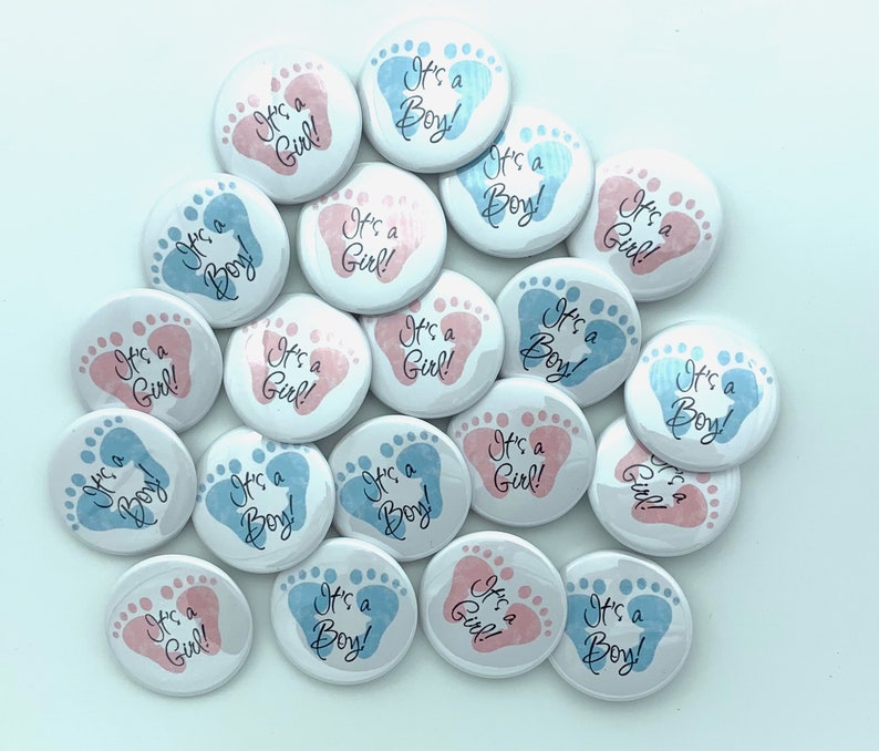 May include: A collection of 18 round baby shower buttons with blue and pink footprints. The buttons have the text "It's a Boy!" or "It's a Girl!" printed on them.