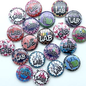 May include: A collection of 16 colorful round buttons with various science-themed designs. Each button features the word "LAB" in a different font and style. The buttons are decorated with images of beakers, test tubes, microscopes, and other science-related symbols.