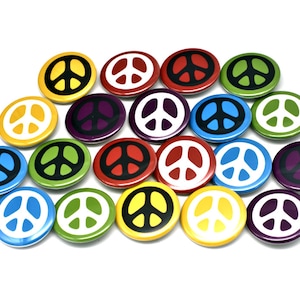 May include: A collection of 17 peace sign buttons in various colors, including red, yellow, green, blue, and purple. The buttons are all round and have a white peace sign in the center.