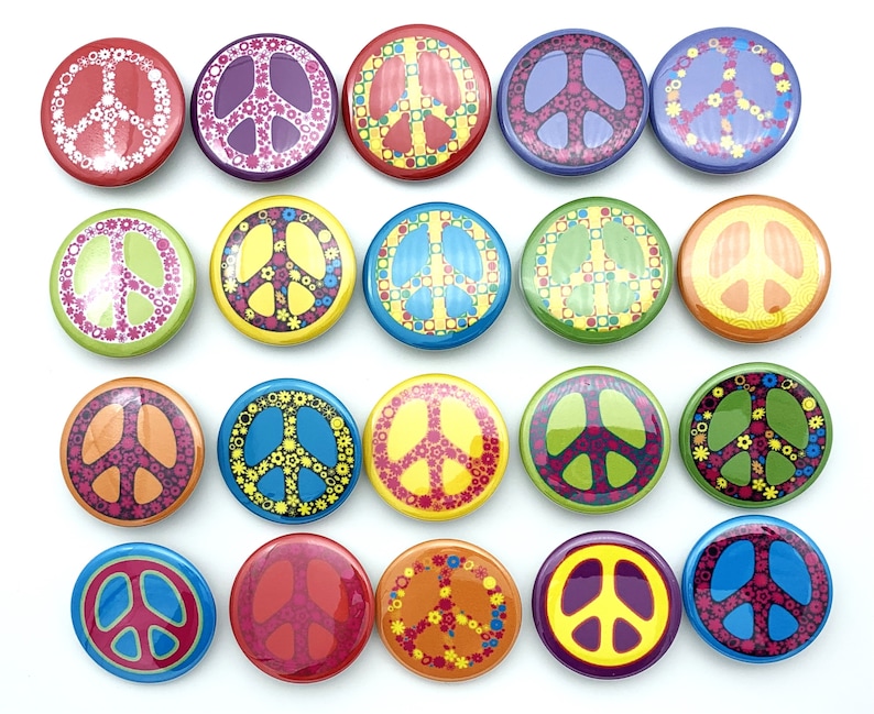 May include: A collection of 18 round peace sign buttons with various colorful designs. The buttons feature a peace sign symbol with different patterns and colors, including red, blue, green, yellow, and orange.