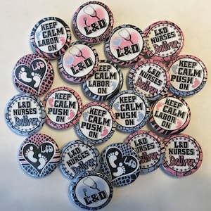 May include: A collection of round buttons with various designs and text. Some buttons feature the text "KEEP CALM LABOR ON" and "KEEP CALM PUSH ON" with baby footprints. Others display "L&D Nurses Deliver" and "L&D" with a stethoscope. The buttons have pink, blue, and black accents.