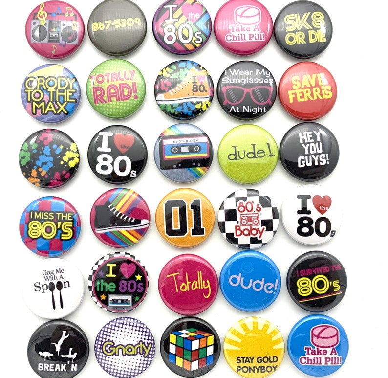 May include: A collection of 20 colorful 1-inch button pins with various 1980s themed designs. The pins feature text, images, and graphics related to the 1980s, including the words "I love the 80s", "Totally Rad", "Save Ferris", "Gnarly", "Dude", "Break'n", "Stay Gold Ponyboy", "Take a Chill Pill", and "80's Baby".