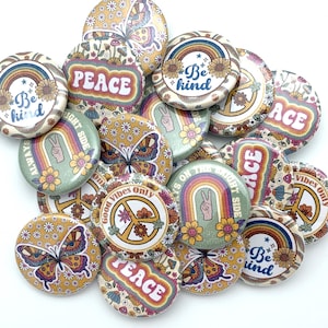 May include: A collection of 15 round, colorful buttons with various designs. The buttons feature peace signs, rainbows, butterflies, and text such as "Peace", "Be Kind", and "Good Vibes Only".
