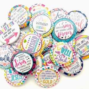 May include: A collection of colorful round buttons with inspirational quotes and bible verses. The buttons feature a variety of designs and colors, including pink, blue, green, yellow, and purple. The text on the buttons includes phrases such as "Walk by Faith", "It is Well with My Soul", "Blessed Assurance", and "You are Altogether Beautiful".