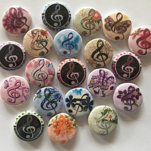 May include: A collection of 17 round buttons with various floral and abstract designs featuring a treble clef. The buttons are in shades of pink, blue, green, purple, and black.