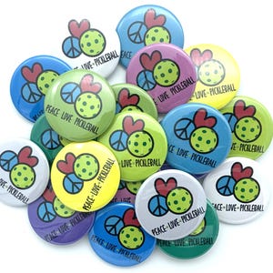 May include: A collection of colorful round buttons with a peace sign, a heart, and a pickleball. The buttons have the text "Peace Love Pickleball" on them.