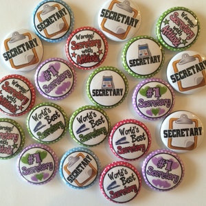May include: A collection of 16 colorful round buttons with various designs and text related to the role of a secretary. Some buttons feature the word "Secretary" with a clipboard icon, while others have phrases like "World's Best Secretary" and "Warning! Secretary with Attitude".