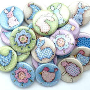 May include: A collection of 15 colorful round buttons with various animal and floral designs. The buttons feature a blue bird, a pink bunny, a blue bunny, a sheep, a red chicken, a blue penguin, and a flower with a heart.