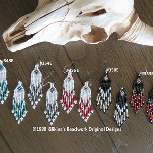 May include: Five pairs of beaded earrings in various colors, including black, white, red, and teal. The earrings are all in the same style, with a teardrop shape and a fringe of beads. The earrings are displayed on a wooden surface with a white animal skull in the background. The text "©1989 Kilikina's Beadwork Original Designs" is visible at the bottom of the image.