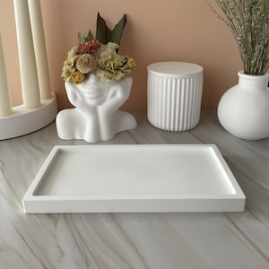 May include: White ceramic tray with a raised edge. The tray is empty and is sitting on a light brown surface.