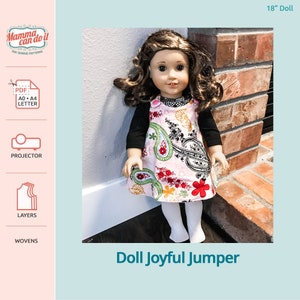 May include: A pink and green paisley print doll jumper with black straps and buttons. The jumper is being worn by a doll with brown hair and blue eyes. The doll is standing in front of a brick wall. The text "Doll Joyful Jumper" is printed below the image.