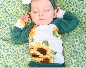 May include: A baby wearing a white and green long-sleeved shirt with a sunflower print. The shirt has a green raglan sleeve. The baby is wearing a white headband with a sunflower bow. The baby is lying on a green and blue floral sheet.  PDF: Sewing Pattern + Layers