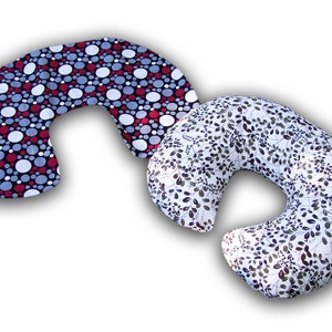 May include: Two crescent-shaped pillows. One pillow features a black background with red, white, and gray polka dots. The other pillow has a white background with a pattern of dark green leaves and stems.