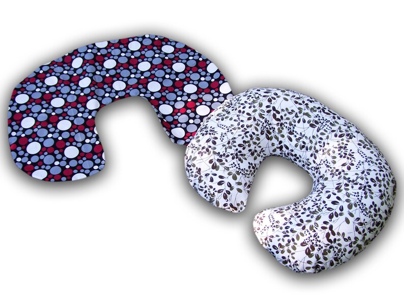 May include: Two crescent-shaped pillows. One pillow features a black background with red, white, and gray polka dots. The other pillow has a white background with a pattern of dark green leaves and stems.