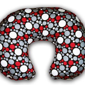 May include: A U-shaped nursing pillow with a black background and a pattern of red, white, and gray circles of varying sizes. The pillow is designed for comfort and support during breastfeeding.