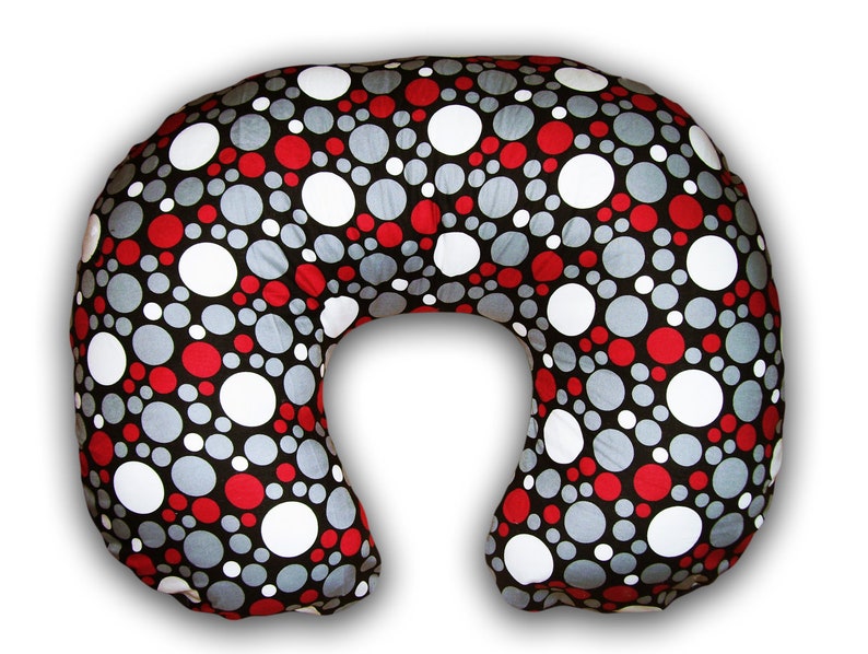 May include: A U-shaped nursing pillow with a black background and a pattern of red, white, and gray circles of varying sizes. The pillow is designed for comfort and support during breastfeeding.