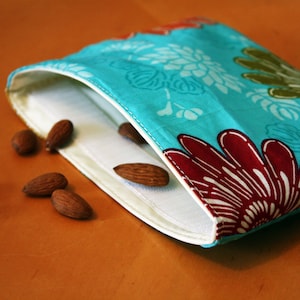 May include: A turquoise fabric pouch with a floral pattern in shades of red, white, and green. The pouch is open and has almonds inside.