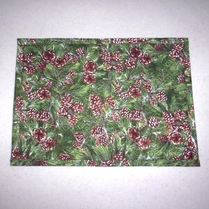 May include: A rectangular fabric item with a repeating pattern of green pine needles and brown pine cones. The fabric has a festive, holiday theme, suitable for seasonal decor or crafts.