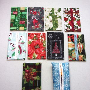 May include: A collection of ten rectangular fabric tissue holders featuring various holiday-themed patterns, including Christmas trees, poinsettias, snowmen, ornaments, holly, and snowflakes in vibrant red, green, blue, black, and white colors.