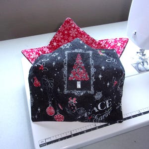 May include: A fabric bowl cozy featuring a black exterior with a Christmas tree, ornaments, and the word PEACE, and a red interior with a white snowflake pattern. The cozy sits on a white sewing machine base with a visible ruler measuring 8 inches.