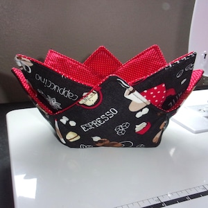 May include: A handmade fabric bowl with a black exterior featuring coffee-themed graphics and the words "Cappuccino" and "Espresso." The interior is red with white polka dots. The bowl is designed with a unique, petal-like shape.