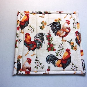 May include: Square quilted fabric with a rooster pattern. The fabric features colorful roosters in red, orange, and black, interspersed with floral designs on a cream background. The edges are neatly stitched.