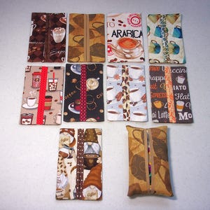 May include: Ten rectangular fabric tissue holders arranged in three rows. Each holder features a unique coffee-themed pattern, including cups, beans, and gnomes. The designs incorporate various colors like brown, cream, red, and blue, with central openings.