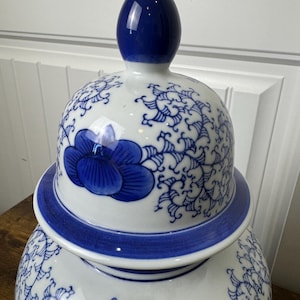 Könnte beinhalten: Eine weiß-blaue Keramik-Ingwer-Vase mit Deckel. Die Vase hat ein blaues Blumenmuster und eine blaue Blume auf dem Deckel. Der Deckel hat einen dunkelblauen Knopf.