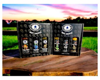Könnte beinhalten: Zwei schwarze Geschenkboxen mit Totenkopfmotiven und dem Text "Core Punk Hot Sauces" auf der Vorderseite. Jede Box enthält drei kleine Glasflaschen mit scharfer Sauce mit bunten Etiketten, auf denen Comicfiguren und Namen wie "Pinco Pingo", "Blue-Fi", "Killer Kai", "Core Punk", "Core Punk" und "Haizenz" abgebildet sind.