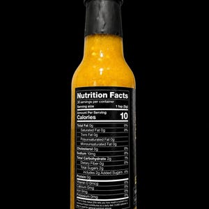 Op de afbeelding: Een doorzichtige glazen fles gevuld met een felgeel-oranje saus, afgesloten met een zwarte dop. Een zwart etiket aan de voorzijde toont de voedingswaarde, met 10 calorie&euml;n per portie van 5g en 30 porties per verpakking.