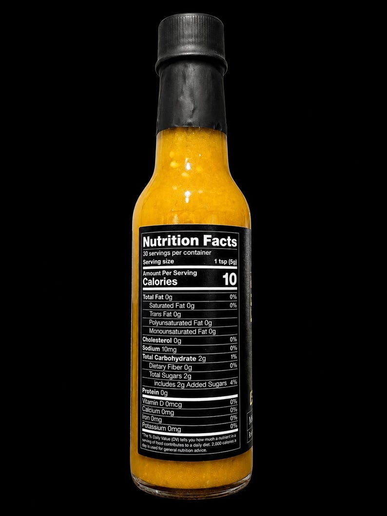 Op de afbeelding: Een doorzichtige glazen fles gevuld met een felgeel-oranje saus, afgesloten met een zwarte dop. Een zwart etiket aan de voorzijde toont de voedingswaarde, met 10 calorie&euml;n per portie van 5g en 30 porties per verpakking.