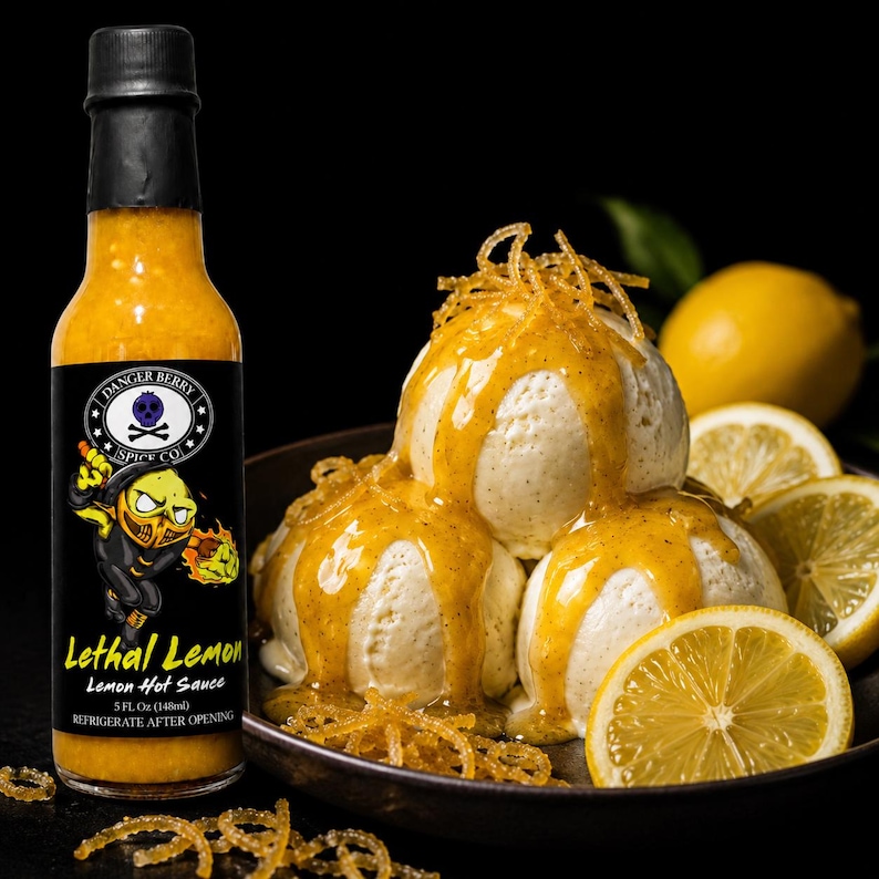 Op de afbeelding: Een glazen fles Danger Berry Spice Co. Lethal Lemon hete saus met een zwarte dop en een etiket met een geel citroenhoofd-figuur. Daarnaast drie bollen vanille-ijs overgoten met gele hete saus en citroenrasp.