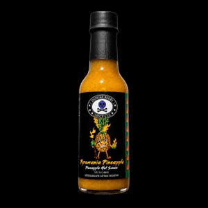 K&ouml;nnte beinhalten: Eine klare Glasflasche mit Pyromania Pineapple scharfer So&szlig;e und schwarzem Verschluss. Das Etikett zeigt eine animierte Ananasfigur mit Flammen, ein Totenkopf-Logo und den Text Danger Berry Spice Co. Die Flasche enth&auml;lt 148 ml der So&szlig;e.