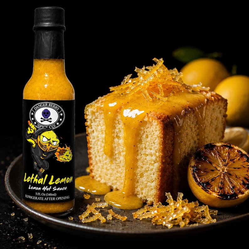 Op de afbeelding: Een glazen fles Lethal Lemon hete saus van Danger Berry Spice Co. met een zwarte dop en een etiket met een gele stripfiguur. De fles bevat 148 ml gele saus en staat naast een plak cake met een glazuurlaag van citroen.