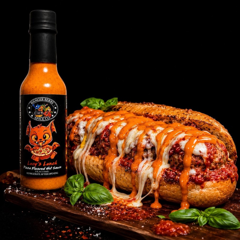May include: A bottle of Danger Berry Spice Co. Lucy's Lunch pizza flavored hot sauce next to a meatball sub on a toasted baguette, topped with melted white cheese, red tomato sauce, and drizzled with orange hot sauce, garnished with basil.