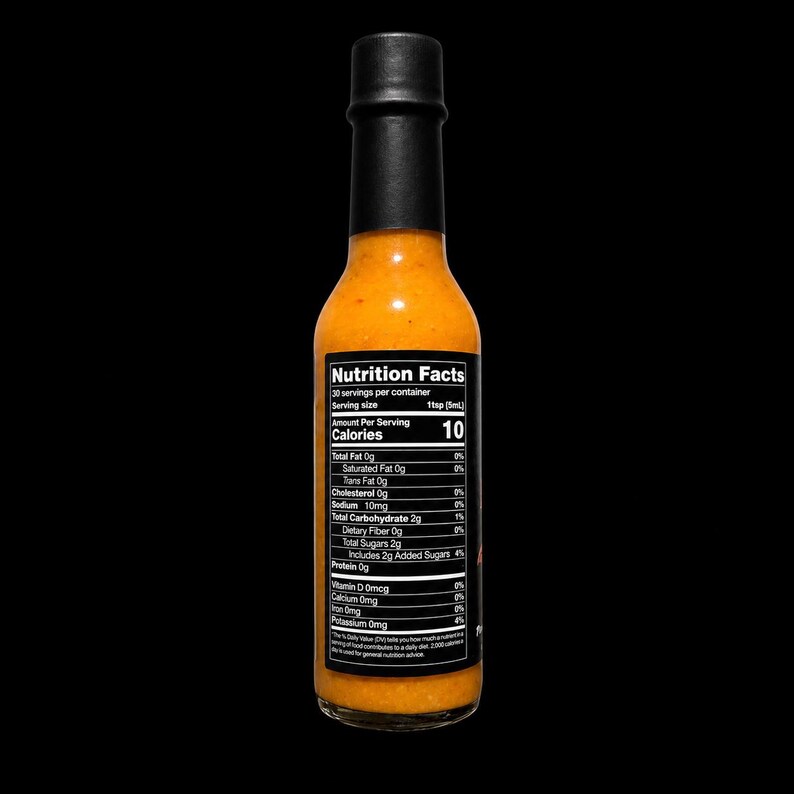 May include: A clear glass bottle filled with orange hot sauce, topped with a black cap. A black rectangular nutrition facts label is applied to the front, displaying text including 10 calories per serving and 30 servings per container.