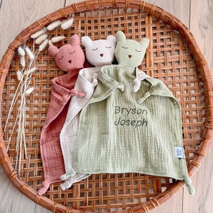May include: A green, cream, and pink muslin baby security blanket with three attached animal head toys. The blanket is personalized with the name "Bryson Joseph".