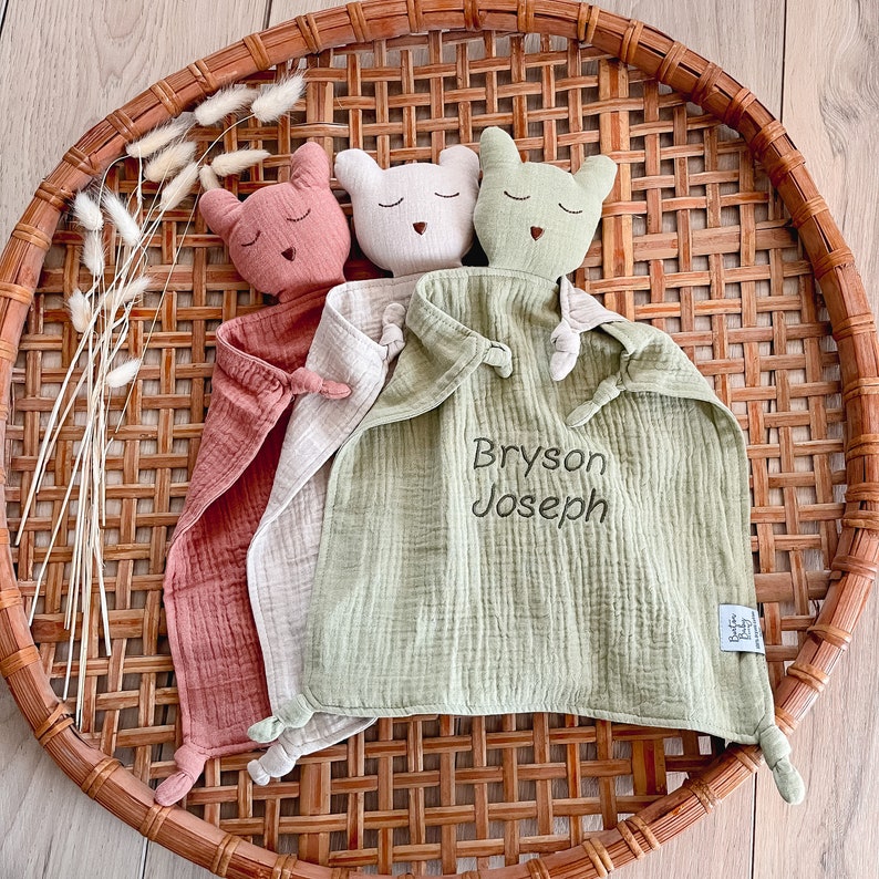 May include: A green, cream, and pink muslin baby security blanket with three attached animal head toys. The blanket is personalized with the name "Bryson Joseph".
