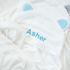 May include: White hooded towel with blue ear appliques and the name "Asher" embroidered in blue thread.