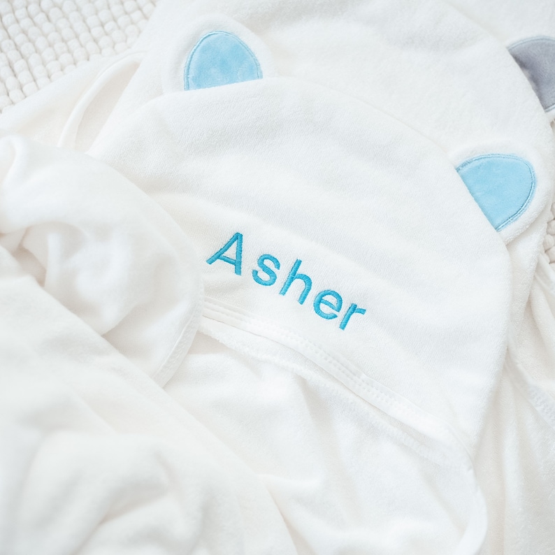 May include: White hooded towel with blue ear appliques and the name "Asher" embroidered in blue thread.