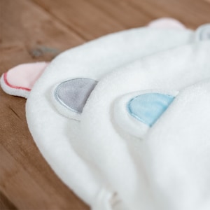 May include: Three white hooded towels with embroidered ears. The ears are pink, gray, and blue.