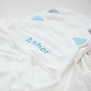 May include: White hooded towel with blue ears and the name "Asher" embroidered in blue thread.