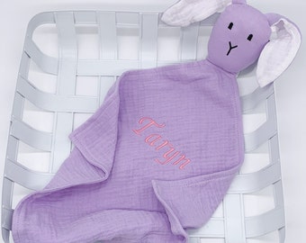Può includere: Una copertina di sicurezza per bambini di colore lavanda con una testa di coniglio attaccata. La copertina è ricamata con il nome "Layla".