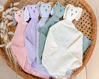 Può includere: Cinque coperte di sicurezza in peluche a forma di coniglio in diversi colori, tra cui rosa, viola, verde, crema e blu. La coperta crema ha il nome "Jack" ricamato.