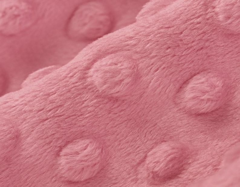 May include: Close-up of a soft, pink fabric with a textured, dotted pattern. The fabric is plush and has a subtle sheen.