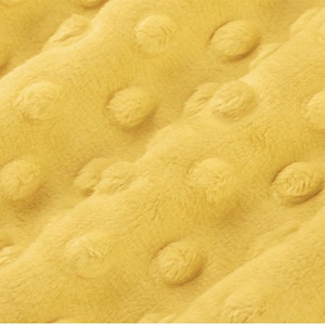 May include: Close-up of a soft, yellow blanket with a textured, dotted pattern. The plush fabric has a fuzzy, tactile appearance. The blanket's color is a bright, sunny yellow, and the raised dots create a dimensional effect.