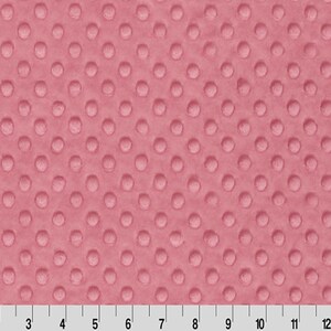 May include: A close-up of a pink minky fabric with a textured dot pattern. The fabric is soft and plush, perfect for baby blankets, throws, and other projects.