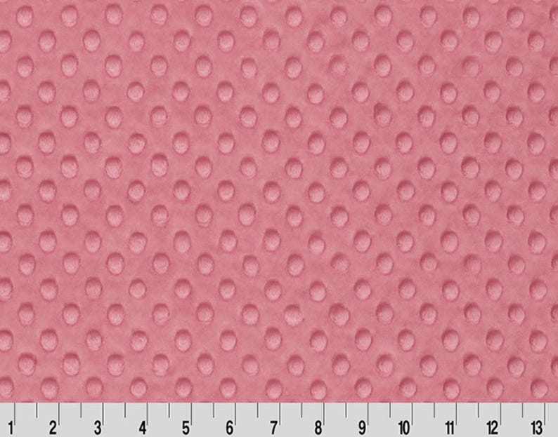 May include: A close-up of a pink minky fabric with a textured dot pattern. The fabric is soft and plush, perfect for baby blankets, throws, and other projects.