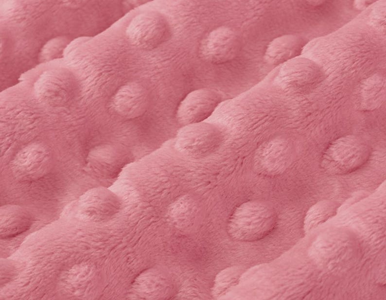 May include: Close-up of a soft, pink fabric with a textured, dotted pattern. The fabric is plush and has a subtle sheen.