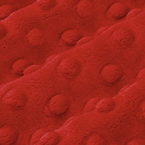 May include: Close-up of a vibrant red fabric with a textured, raised dot pattern. The plush material is soft and appears to be a blanket or throw, with a cozy and inviting appearance. The fabric's texture creates shadows and highlights.